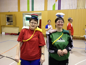Zwei Behindertensportlerinnen balancieren lachend kleine farbige Kissen auf dem Kopf